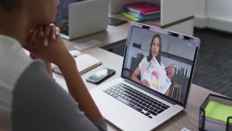 Mid-section-of-african-american-woman-having-a-video-call-on-laptop-with-female-colleague-at-office
