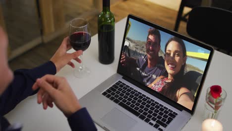 Mid-section-of-african-american-woman-holding-wine-glass-while-having-a-video-call-on-laptop-at-home