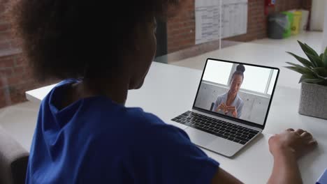 Back-view-of-african-american-woman-having-a-video-call-on-laptop-with-female-colleague-at-office