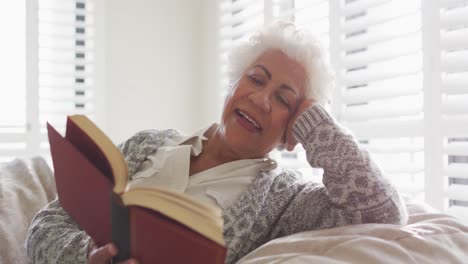 Eine-Afroamerikanische-Seniorin-Lächelt,-Während-Sie-Zu-Hause-Auf-Einem-Sitzsack-Sitzt-Und-Ein-Buch-Liest