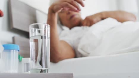 Sick-african-american-senior-woman-drinking-water-while-lying-on-the-bed-at-home