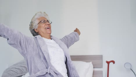 Afroamerikanische-Seniorin-Streckt-Ihre-Arme-Aus,-Während-Sie-Zu-Hause-Auf-Dem-Bett-Sitzt