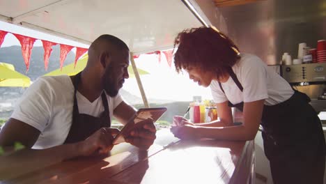 African-american-couple-wearing-aprons-using-digital-tablet-and-taking-notes-in-the-food-truck