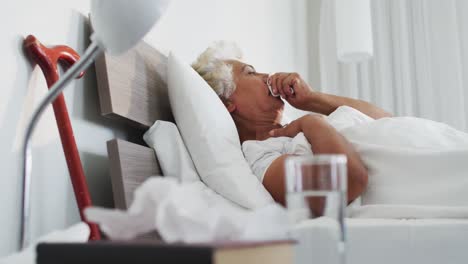 Sick-african-american-senior-woman-holding-tissue-coughing-while-lying-on-the-bed-at-home