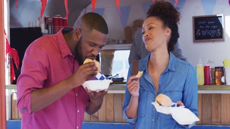 Pareja-Afroamericana-Comiendo-Hamburguesas-Y-Papas-Fritas-Juntos-En-El-Camión-De-Comida