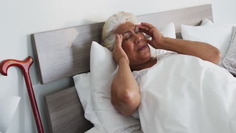 Kranke-Afroamerikanische-Seniorin-Hält-Ihren-Kopf,-Während-Sie-Zu-Hause-Auf-Dem-Bett-Liegt