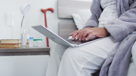 Mid-section-of-african-american-senior-woman-using-laptop-while-sitting-on-the-bed-at-home