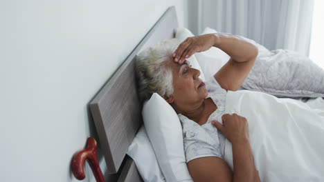 Kranke-Afroamerikanische-Seniorin-Hält-Ihren-Kopf,-Während-Sie-Zu-Hause-Auf-Dem-Bett-Liegt