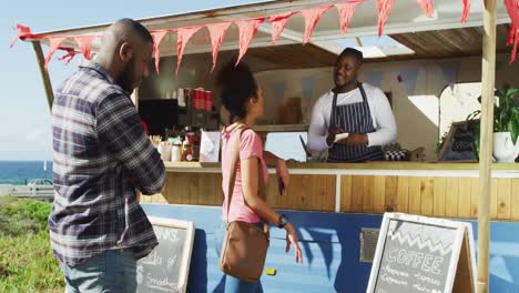 Smiling-african-american-male-food-truck-owner-taking-order-from-woman,-and-man-waiting-in-queue