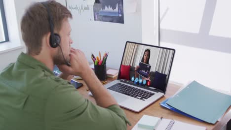 Caucasian-man-wearing-phone-headset-having-a-video-call-with-female-colleague-on-laptop-at-office
