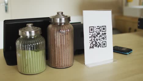 Spices-in-jars,-plaque-with-qr-code-and-smartphone-lying-on-countertop
