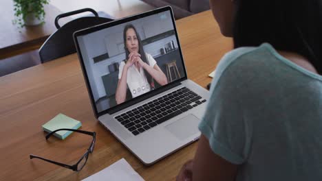 Mixed-race-businesswoman-sitting-at-desk-using-laptop-having-video-call-with-female-colleague