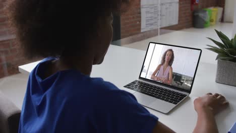 Back-view-of-african-american-woman-having-a-video-call-with-female-colleague-on-laptop-at-office