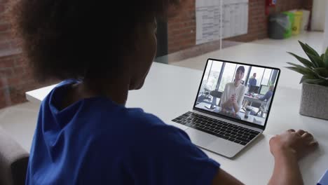 Back-view-of-african-american-woman-having-a-video-call-with-female-colleague-on-laptop-at-office