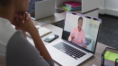 Mid-section-of-african-american-woman-having-a-video-call-with-male-colleague-on-laptop-at-office