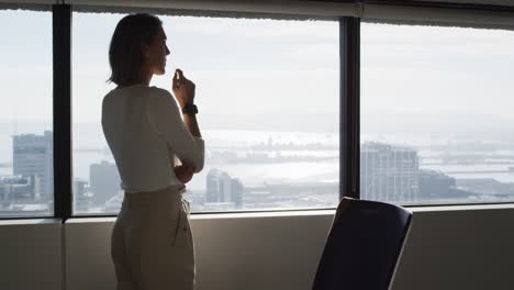 Back-view-of-caucasian-businesswoman-standing-at-window-and-thinking