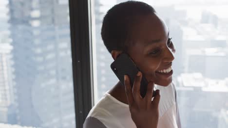 Portrait-of-smiling-african-american-businesswoman-having-call-at-window