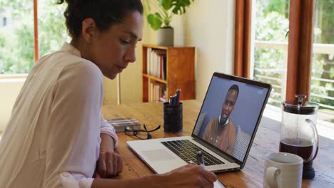 Mixed-race-businesswoman-sitting-at-desk-using-laptop-having-video-call-with-male-colleague