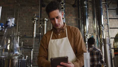 Caucasian-man-working-at-gin-distillery,-using-digital-tablet,-wearing-apron