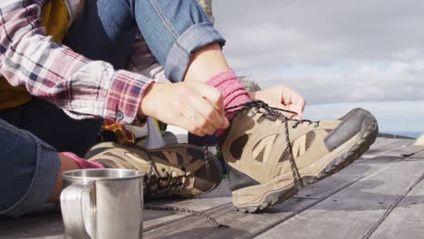 Low-section-of-caucasian-woman-camping,-sitting-outside-tent-putting-on-boots-in-rural-setting