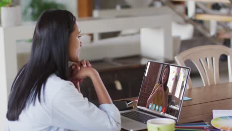 Mixed-race-businesswoman-sitting-at-table-using-laptop-having-video-call-with-female-colleague