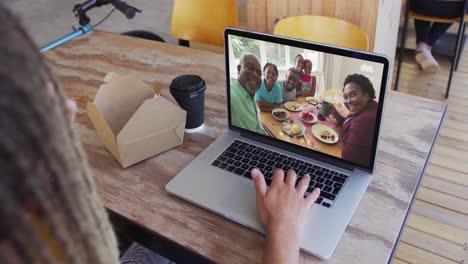Mixed-race-man-sitting-in-cafe-using-laptop-making-video-call-with-family