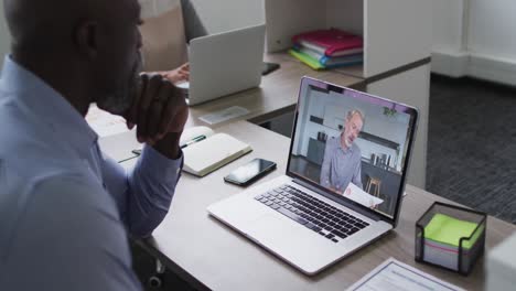 African-american-businessman-sitting-at-desk-using-laptop-having-video-call-with-male-colleague