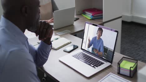 African-american-businessman-sitting-at-desk-using-laptop-having-video-call-with-male-colleague