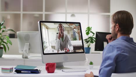 Caucasian-businessman-sitting-at-desk-using-computer-having-video-call-with-male-colleague