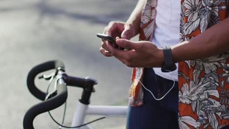 Midsection-of-african-american-man-in-city,-with-bike-in-street-using-smartphone