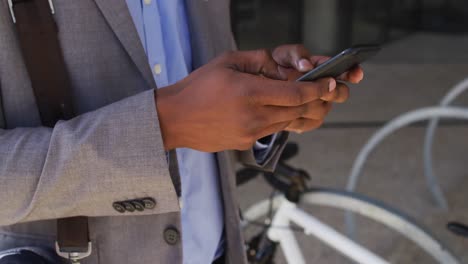 African-american-businessman-using-smartphone-outside-of-modern-office-building