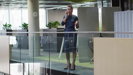 Caucasian-businesswoman-talking-on-smartphone-in-corridor-in-modern-office