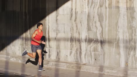 Fit-african-american-man-exercising-in-city,-running-under-bridge