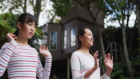 Happy-asian-mother-exercising-in-garden-with-daughter,-practicing-tai-chi-together