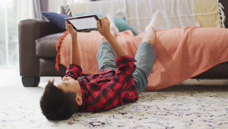Happy-asian-boy-at-home,-lying-on-floor-in-living-room-using-tablet