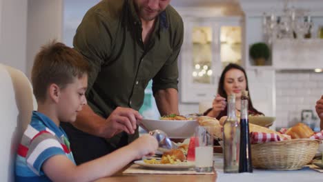 Smiling-caucasian-father-standing-at-table-serving-son-food-before-family-meal