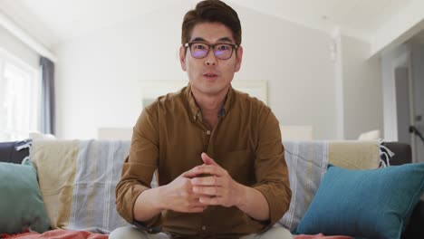 Asian-man-working-at-home,-sitting-on-couch-making-video-call,-talking-and-gesturing