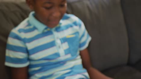 Happy-african-american-boy-sitting-on-couch-reading-book-and-smiling