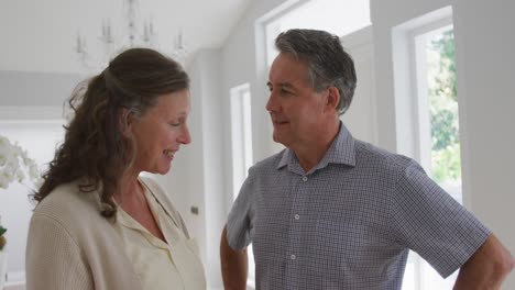 Portrait-of-happy-senior-caucasian-couple-standing-in-living-room-smiling