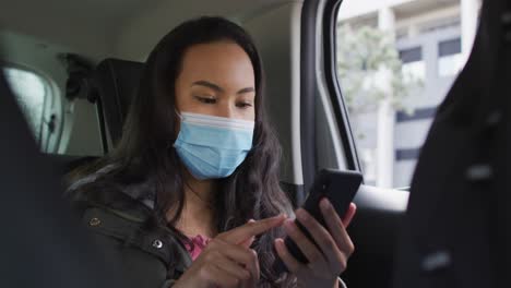 Asiatische-Frau-Trägt-Gesichtsmaske-Und-Benutzt-Smartphone,-Während-Sie-Im-Auto-Sitzt