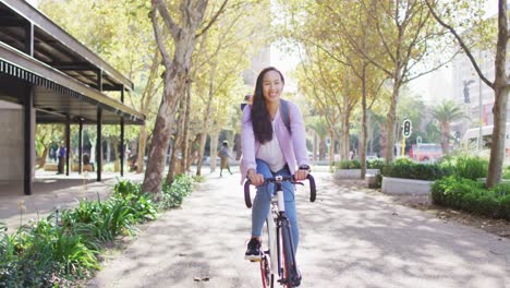 Portrait-of-asian-woman-wearing-backpack-smiling-while-riding-bicycle-on-the-road