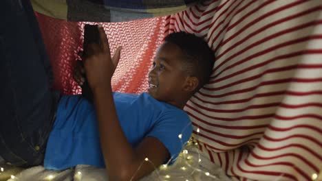 Fröhlicher-Afroamerikanischer-Junge,-Der-Ein-Tablet-Benutzt-Und-Lächelt-Und-Im-Deckenlager-Liegt