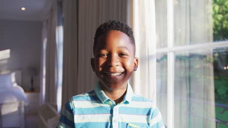Portrait-of-happy-african-american-boy-looking-out-of-sunny-window,-turning-to-camera-and-smiling