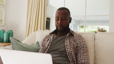 Afroamerikanischer-Mann-Benutzt-Laptop,-Während-Er-Zu-Hause-Auf-Der-Couch-Sitzt