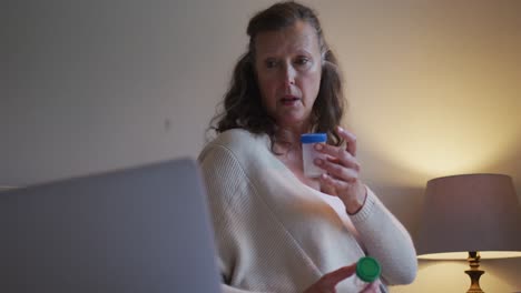 Confused-senior-caucasian-woman-making-consultation-video-call-holding-two-bottles-of-tablets