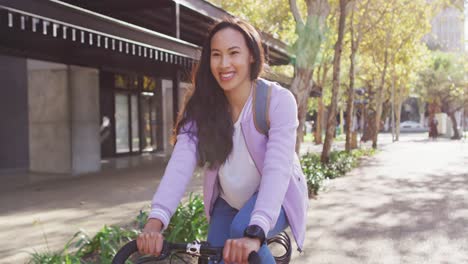 Mujer-Asiática-Con-Mochila-Sonriendo-Mientras-Anda-En-Bicicleta-Por-La-Carretera