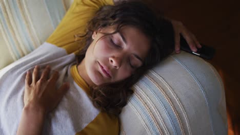 Relaxed-mixed-race-woman-lying-asleep-on-sofa-in-cottage-living-room