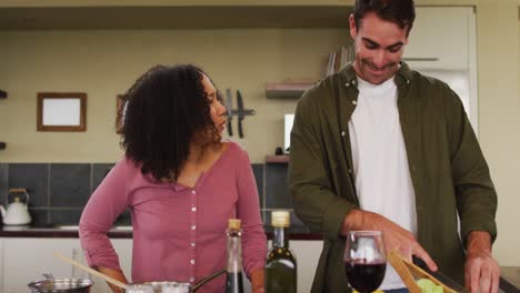 Happy-diverse-couple-preparing-a-meal-together-in-kitchen-and-laughing