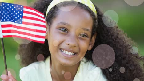 Animation-of-white-circles-moving-over-african-american-girl-holding-american-flag