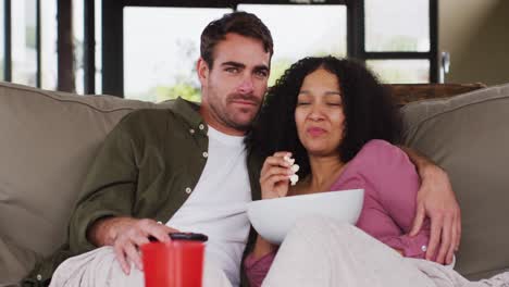 Scared-mixed-race-couple-watching-a-movie-together-sitting-on-the-couch-at-vacation-home